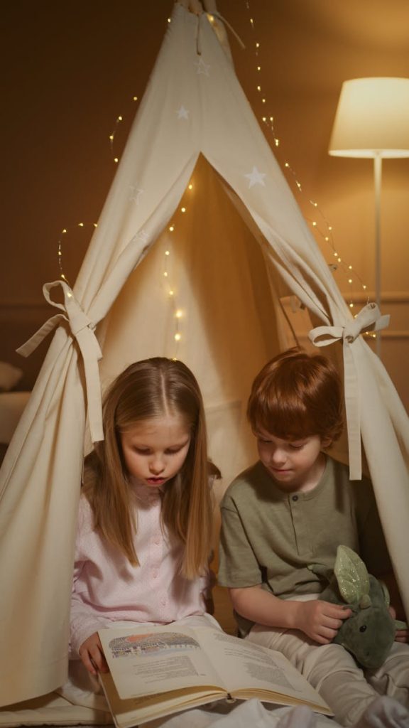 a-boy-and-a-girl-reading-a-book-7494468 Two children reading a book inside a cozy indoor tent lit by fairy lights.